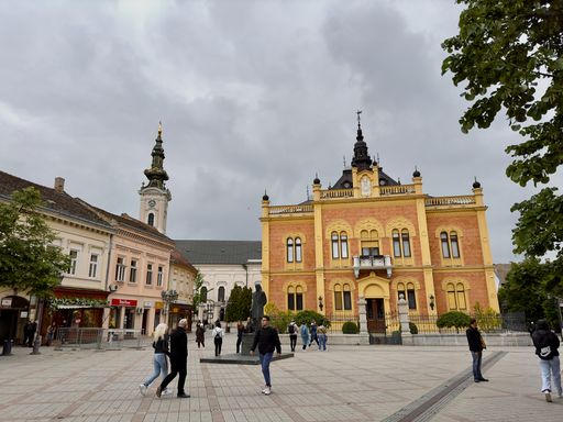 The people strolling in an open square with historical buildings in the background. Novi Sad, Serbia