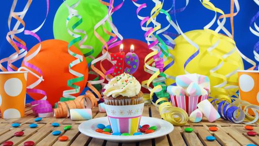Birthday 79 small cupcake with candles burning on rustic wooden table with background of colorful balloons, plastic cups and candies