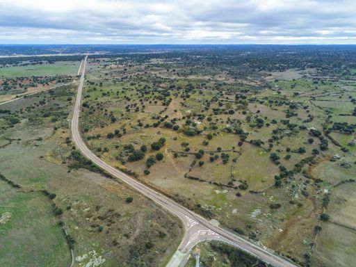 An aerial shot of a road in the middle of grassy fields and trees under a cloudy sky in Salamanca, Spain