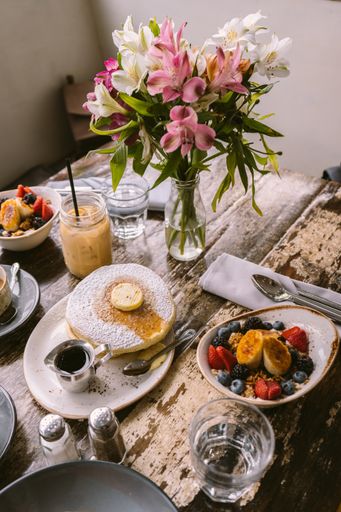 Several types of foods, cookies and drinks put on the table in front of the flower vase