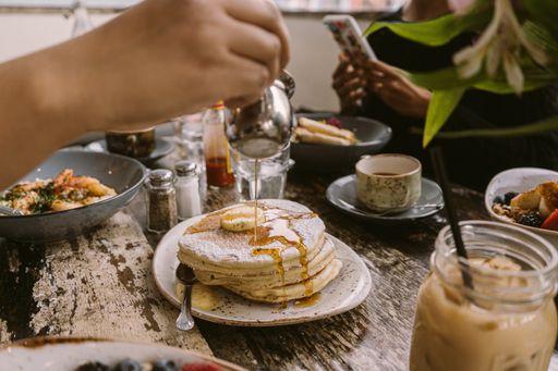 Several pancakes with syrup on the table surrounded with coffee and drinks