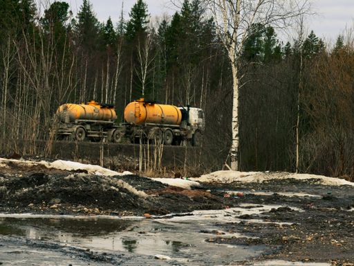 A trailer with a bright orange gas tank rides through a forest on a road in the middle of nowhere in Urals, Russia