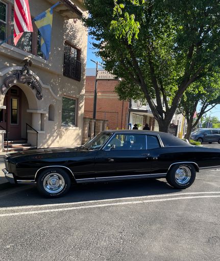 An all black two door retro Monte Carlo Car parked on the street on a sunny day