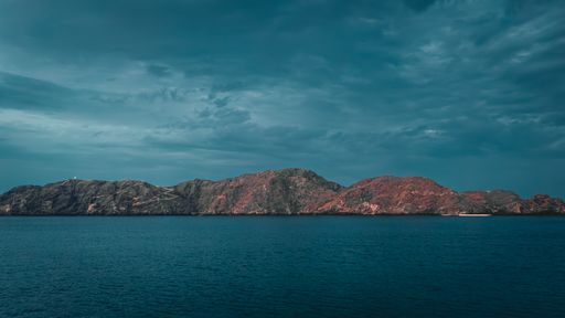 A serene seascape with rocky mountains under a cloudy sky. Muscat, Oman