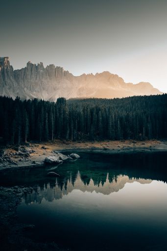 A beautiful shot of the Lake Carezza in Italy, with reflections of trees in the water and amazing mountains in the background