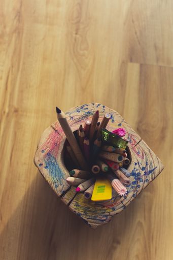 A high angle view of a wooden holder with colourful pencils in it under the lights