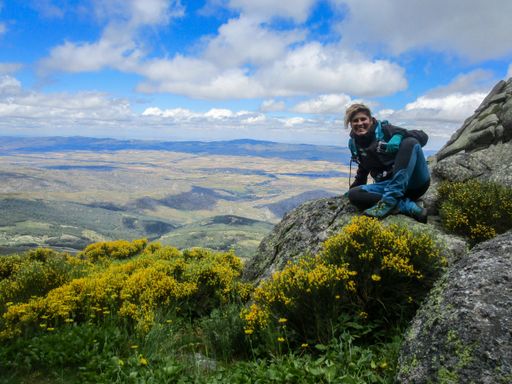 A female Caucasian traveler sitting on a rock on a mountain against a beautiful valley view