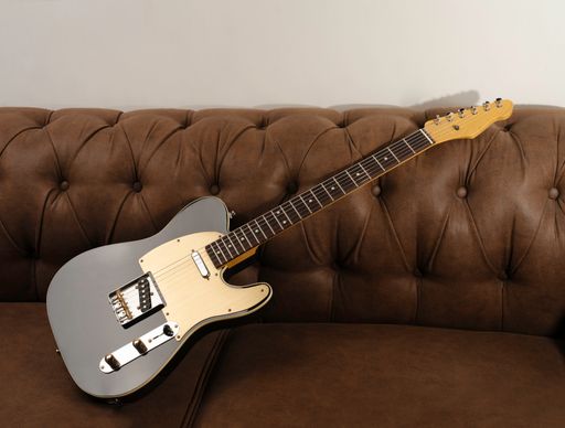 A closeup shot of a handmade electric guitar placed on a brown leather sofa