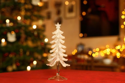 macro of a decoration Christmas tree object made of transprent and white glass in front of blurred Christmassy illuminated room