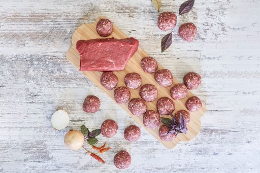 An overhead shot of fresh raw meatballs on a wooden board with ingredients