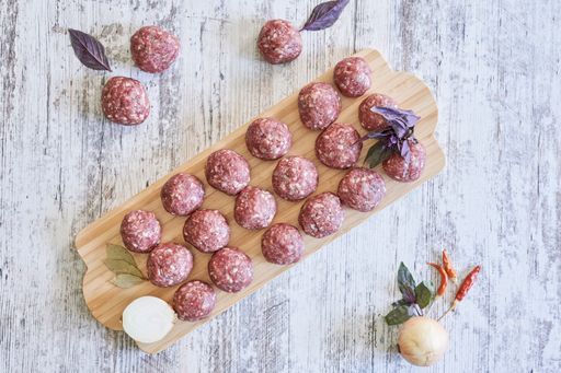An overhead shot of fresh raw meatballs on a wooden board with ingredients