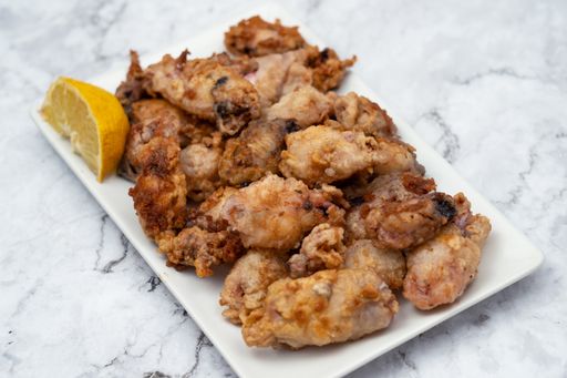 A closeup image of fried chicken on a white plate with lemon on a side over a marble background