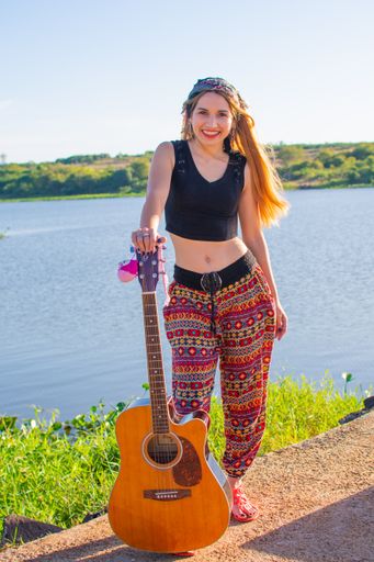 A pretty blonde Argentinian woman with a guitar on her foot posing on the riverside