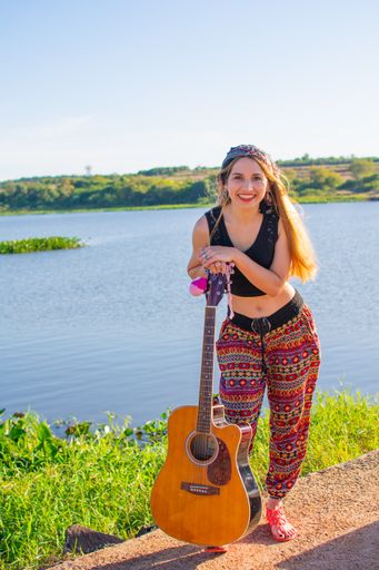A pretty blonde Argentinian woman with a guitar on her foot posing on the riverside