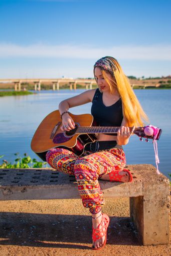 A pretty blonde Argentinian woman sitting on a bench and playing the guitar on the riverside