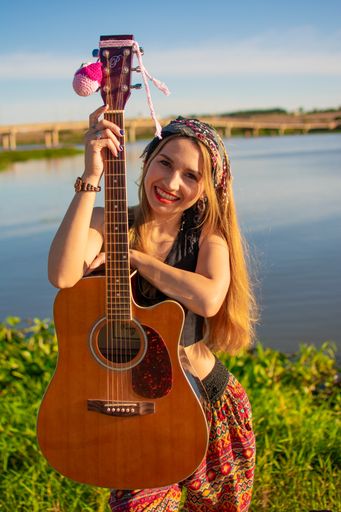 A pretty blonde Argentinian woman with a guitar on her knee posing on the riverside
