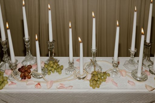 A candlesticks and lit white tapers with grapes, pearls, and pink rose petals.
