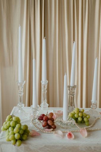 A candlesticks and lit white tapers with grapes, pearls, and pink rose petals.