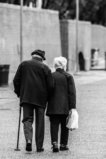 A vertical greyscale shot of an old romantic couple walking holding hands