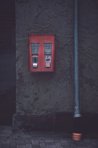 An old classic gumball machine beside a gutter