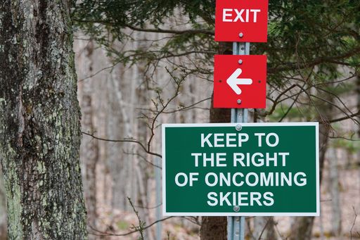 A close-up of forest trail signs: Red exit arrow, keep right for skiers