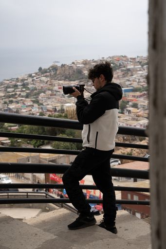 A man in black and white attire capturing photographs on a rooftop