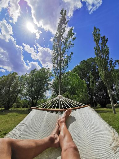 A vertical shot of the legs of a man lying on a hammock in the park and enjoying the sunny day
