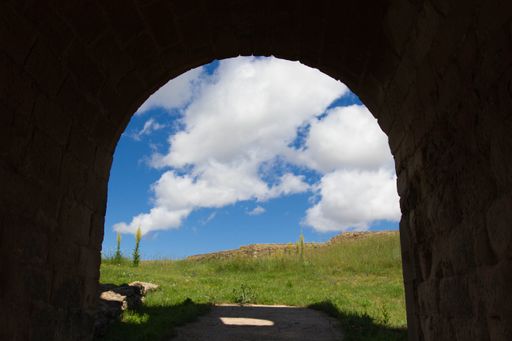 The cloudy sky over the green field captured from an archway
