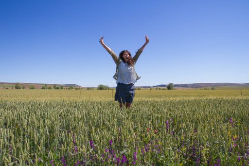 A pretty Spanish woman jumping in the field with wildflowers on a sunny day in summer