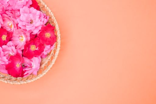A top view of a basket full of vibrant red and pink flowers with copy space next to it on an orange pastel background