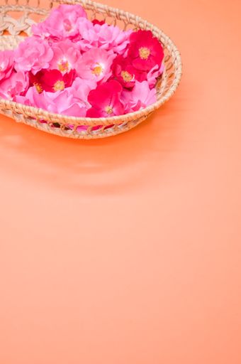 A vertical wallpaper with vibrant red and pink flowers in a basket on a pastel orange background with copy space