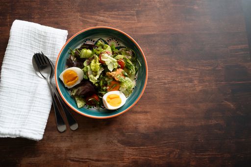 A top view of a salad with eggs and lettuce in a bowl on a wooden table