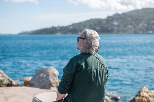 An older man sitting on the shore of the Tuscan port city of Porto Santo Stefano in Italy