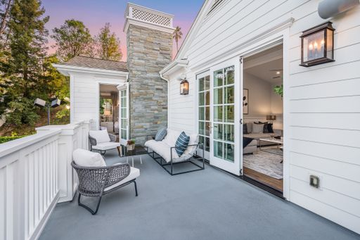 A balcony with a sofa, chairs, and an open door  in a new construction home in Encino, California