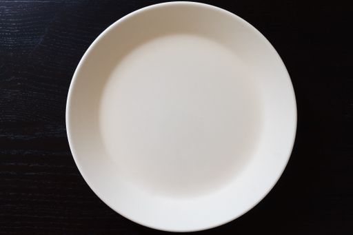 Empty white plate on black wooden table. Kitchen tools close up