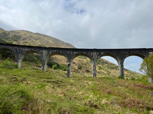 Arched bridge on grassy hill with distant mountains in Scotland