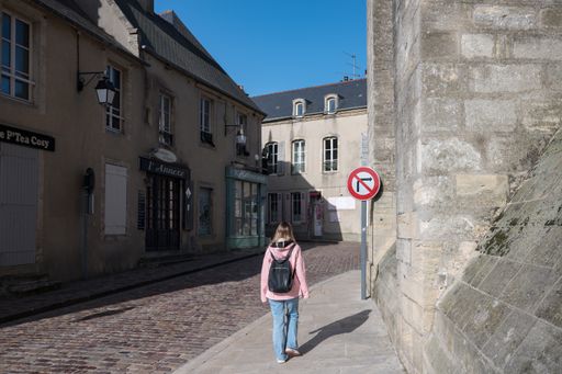 A young blonde girl with a jacket and backpack sightseeing through the picturesque alleys of Bayeux