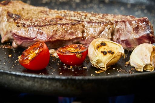 A close up of cooked meat on a black metal frying pan with fried tomato and onions