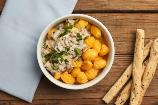 A top view of tasty fresh gnocchi topped with a white sauce with a napkin on a beautiful wooden table