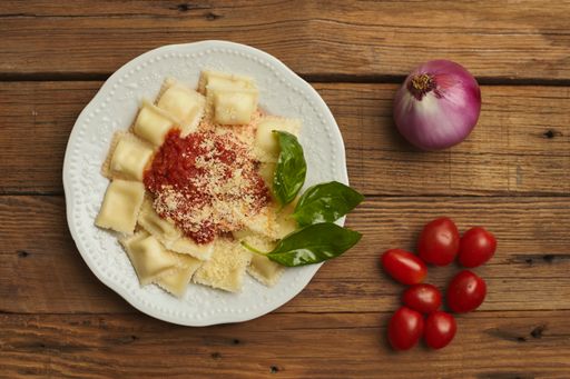 A top view of appetizing ravioli on a ceramic white plate with cherry tomatoes and onion on the side