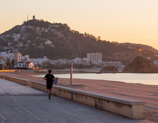 A back shot of a young man black outfit running  beside the beach at sunset with high hills around