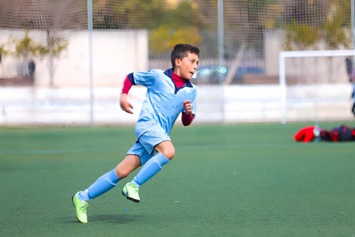 boy playing soccer, sucking the ball on artificial grass during official league match