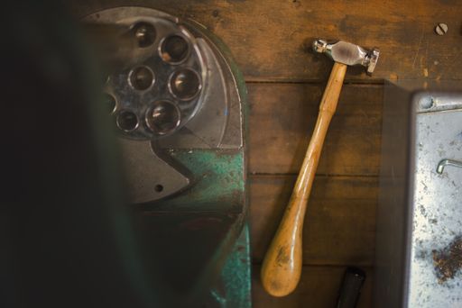Flat lay view of the goldsmith's hammer and six spline ring stretcher and reducer lying on the workshop table.
