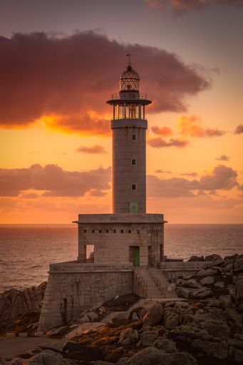 A vertical picture of the Punta Nariga lighthouse surrounded by the sea during the sunset in Spain