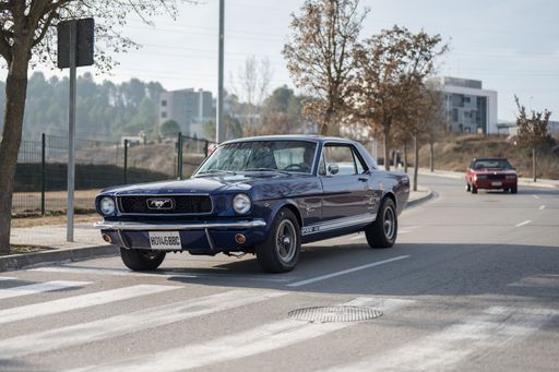 Front view of a beautiful classic American car Ford Mustang first generation V8 289 engine in blue color, it is driving down the street
