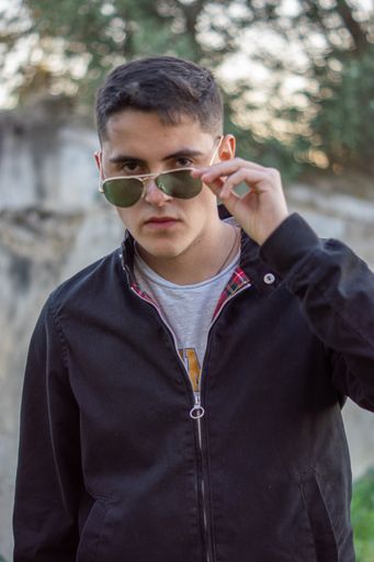 A young man with sunglasses posing for the camera under the sunlight with a blurry background