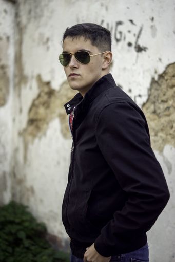 A vertical picture of a man with sunglasses posing for the camera under the sunlight