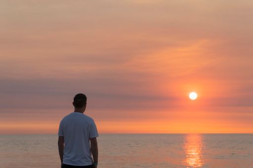 Man standing on beach sand looking towards horizon at orange sunset. Vacation concept. Man reflects looking at the sea.