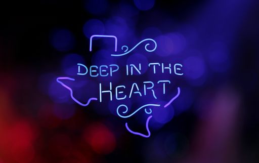 A bright neon illuminated Texas "deep in the heart" sign on a bokeh light background