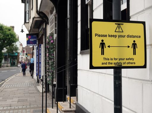 A yellow sign on the High Street to remind people to keep their distance for their safety and the safety of others due to Covid-19.